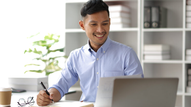 Male Student Studying With Laptop And Writing Down Notes