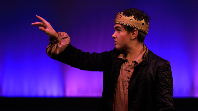 male student wearing a crown in a theater performance