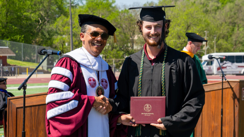 graduate posing with university president at commencement 