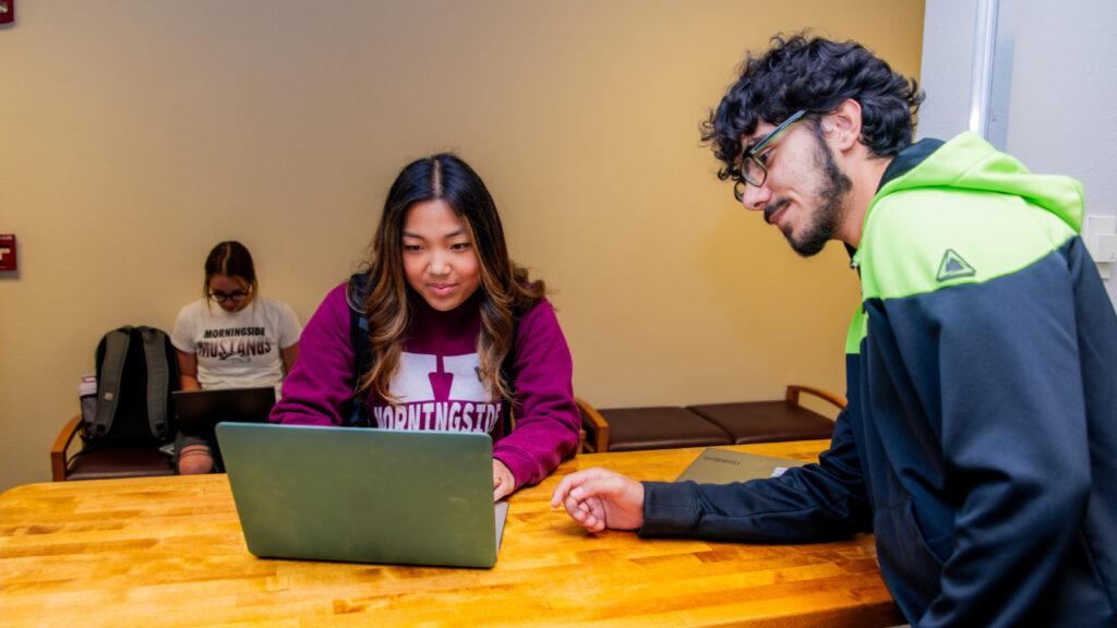 student at IT support desk with her computer while a student waits off to the side.